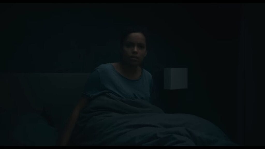 Georgina Campbell as Tess sitting up in bed with a worried expression in a dark bedroom in Barbarian.