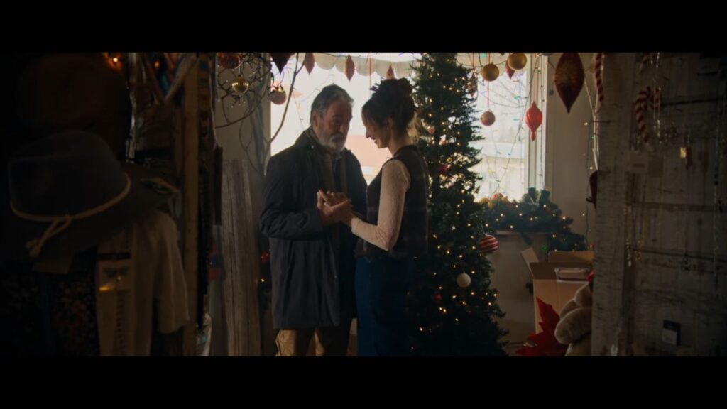 A tender yet sinister moment between characters in an antique shop decked out with festive lights in Silent Night, Deadly Night (2025).