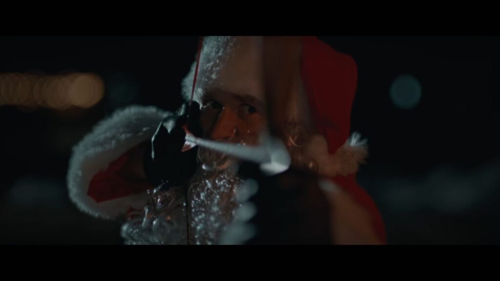 The killer in Silent Night, Deadly Night (2025) dressed as Santa Claus, aiming a bow and arrow directly at the camera.