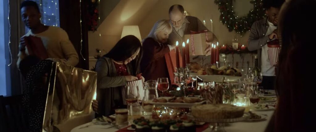 A family gathering around a dinner table exchanging gifts in Twas the Night (2023), one of the more visually polished so-bad-they're-good Christmas horror movies.