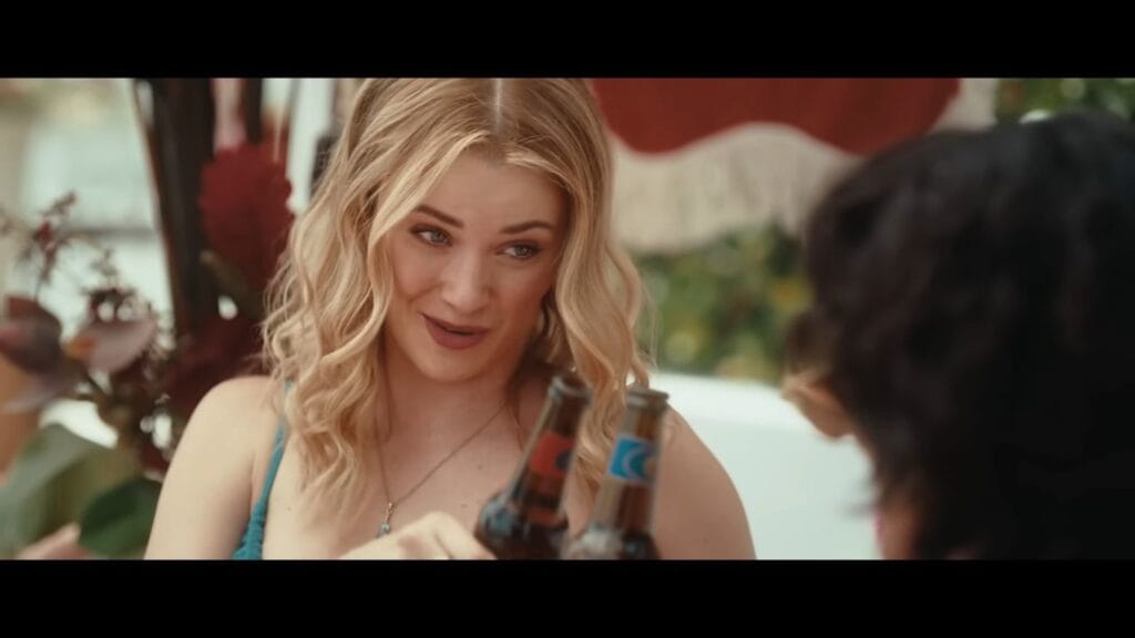 A smiling woman holding two beer bottles during a sunny vacation scene in the movie Killer Whale.