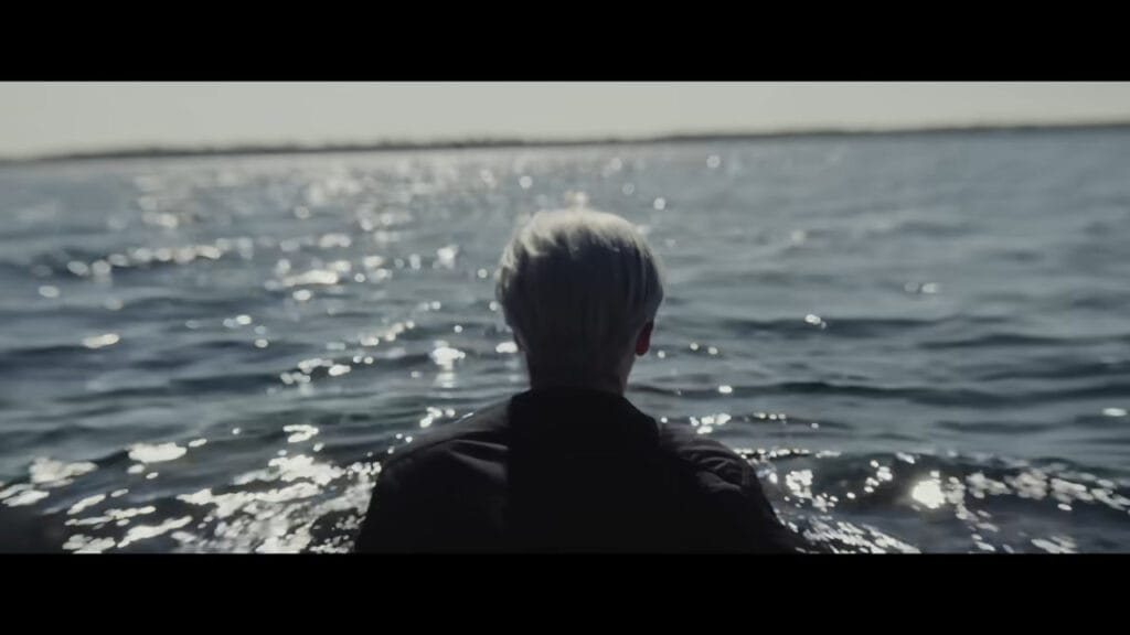 A character looking out over a vast body of water, a key scene from the beginning of The Confession (2025).
