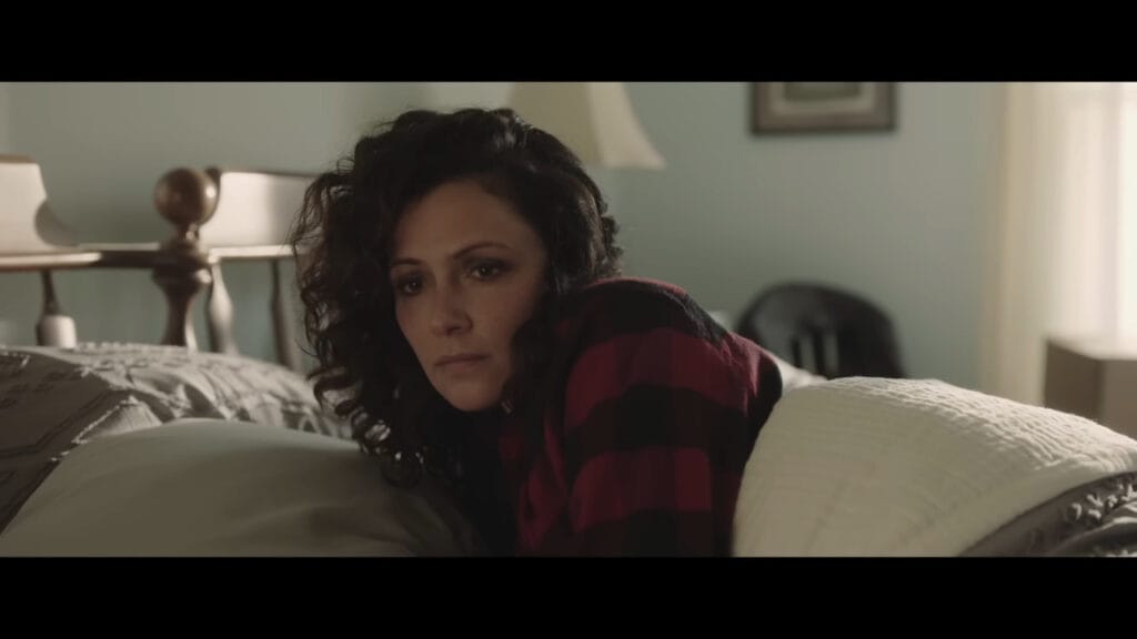 Italia Ricci as a concerned mother lying in bed in a still from the supernatural thriller The Confession (2025).
