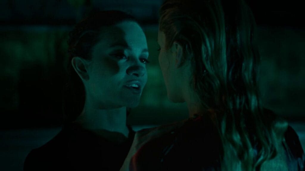 A tense close-up from the movie Twisted (2026) showing Paloma (left) whispering intensely to Smith (right) in a dark, moody setting with green cinematic lighting.