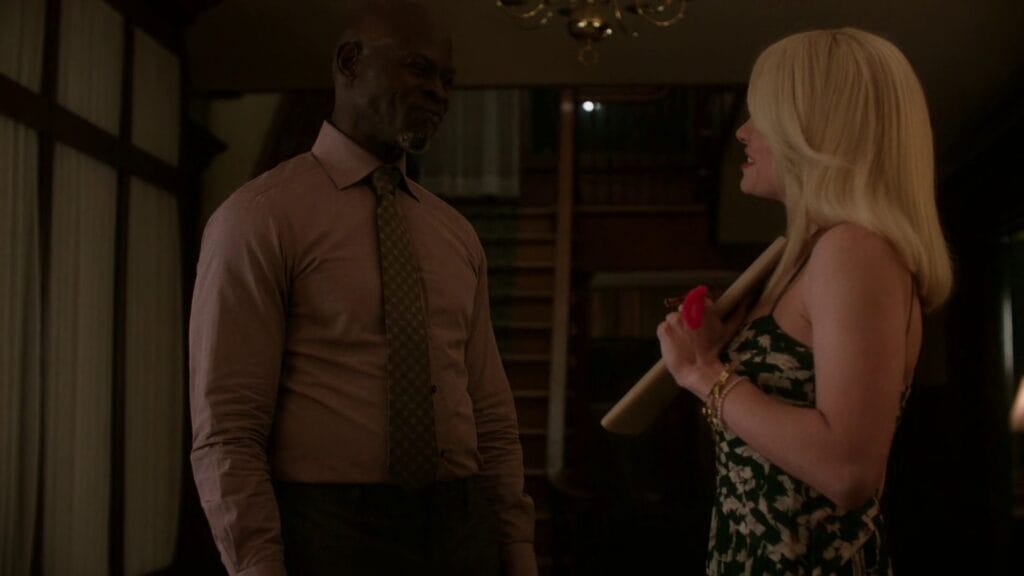 Dr. Kezian standing in a dimly lit, wood-paneled room during a pivotal scene in Twisted. Dr. Kezian wears a professional shirt and tie.