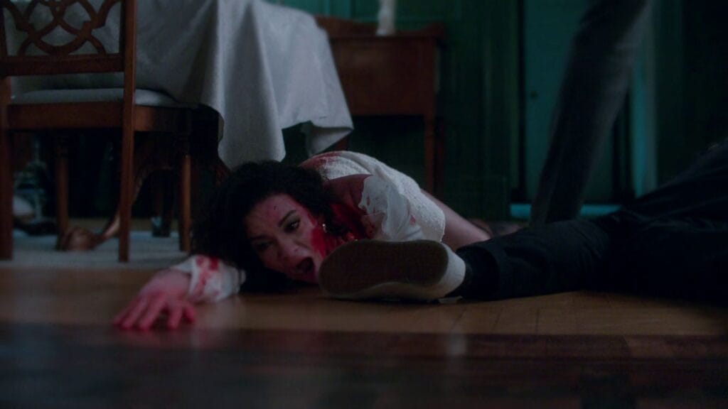 A dramatic shot of Paloma covered in blood, crawling across a hardwood floor in agony during the violent climax of the 2026 movie Twisted.