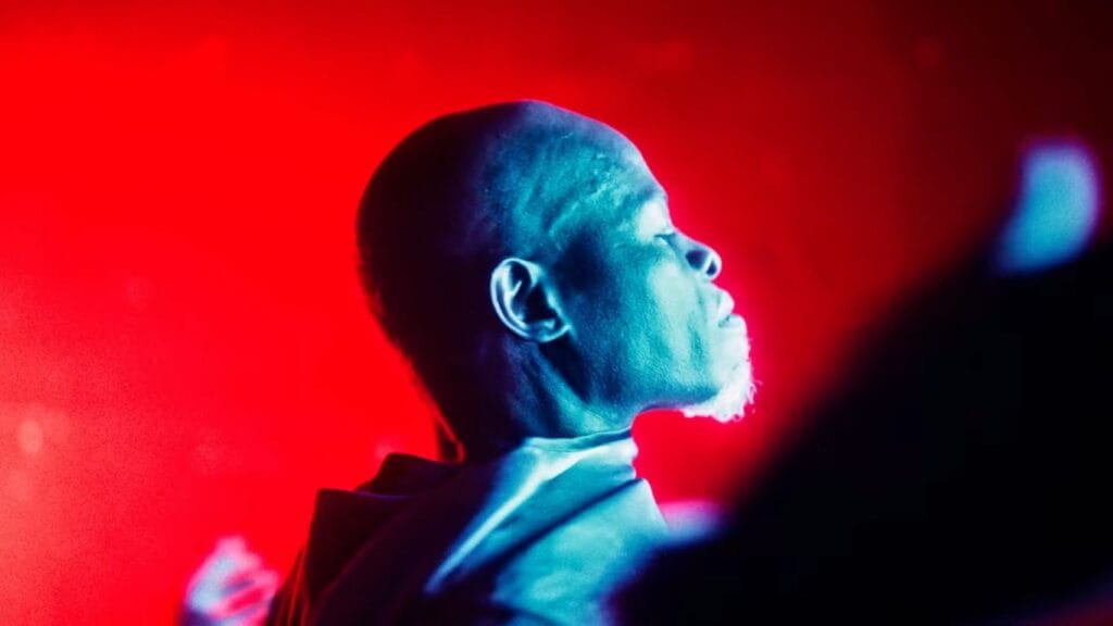 Profile shot of Dr. Kezian (Djimon Hounsou) under harsh, cinematic red and blue lighting, highlighting a serious and dramatic expression.