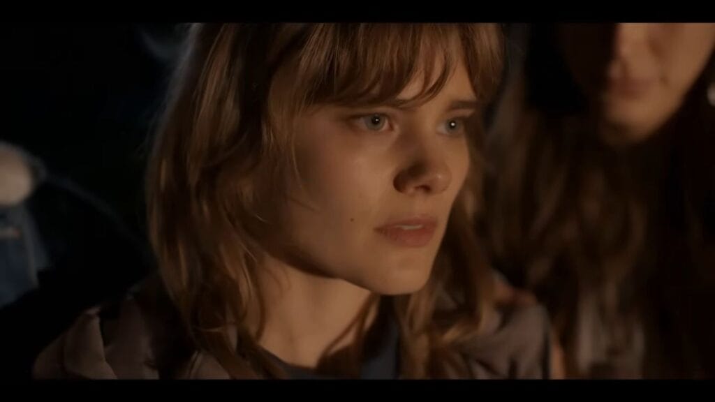 A close-up shot of the lead actress, Elizabeth Cullen, in "Diabolic" (2025). Her face is lit by a warm, orange glow, highlighting a look of intense worry or realization.