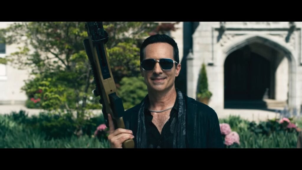One of the wealthy antagonists wearing sunglasses and holding a sniper rifle outside the estate in the horror-comedy sequel Ready or Not 2.