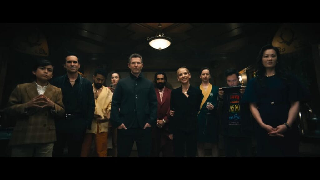 A group of wealthy antagonists, including Sarah Michelle Gellar and Frank Grillo, stand together in a dimly lit hall in Ready or Not 2: Here I Come.