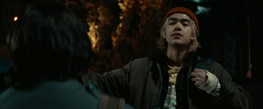 Rel (Sky Yang) wearing an orange beanie and brown jacket looks concerned during a nighttime scene in the Whistle (2025) ending.