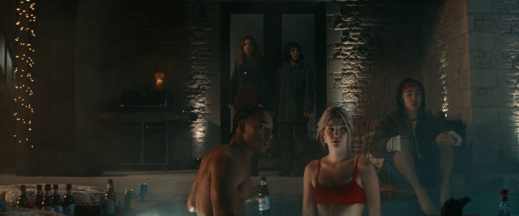 Grace (Ali Skovbye) in a red bikini and Dean (Jhaleil Swaby) look on in terror as Ellie (Sophie Nélisse) and Chrys (Dafne Keen) enter the pool area in Whistle (2025).