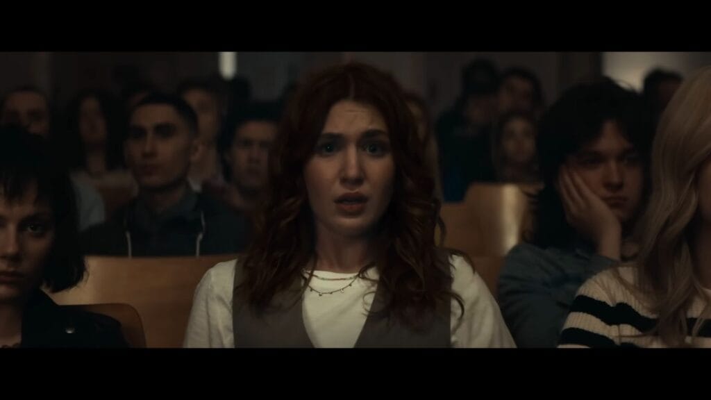 Ellie (Sophie Nélisse) looks shocked and fearful while sitting in a crowded lecture hall in a still from the supernatural horror film Whistle.