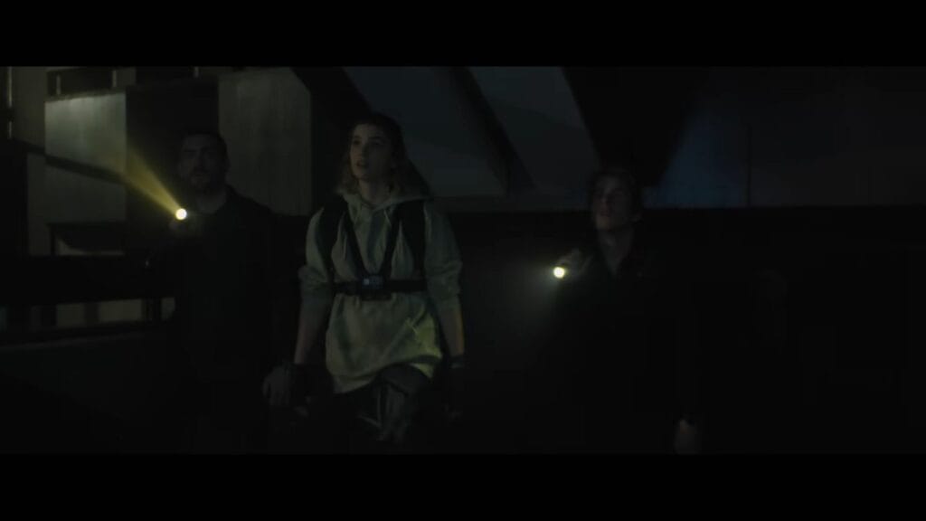 Three urban explorers use flashlights to navigate a dark, abandoned industrial interior in a tense scene from the horror movie Do Not Enter (2026).