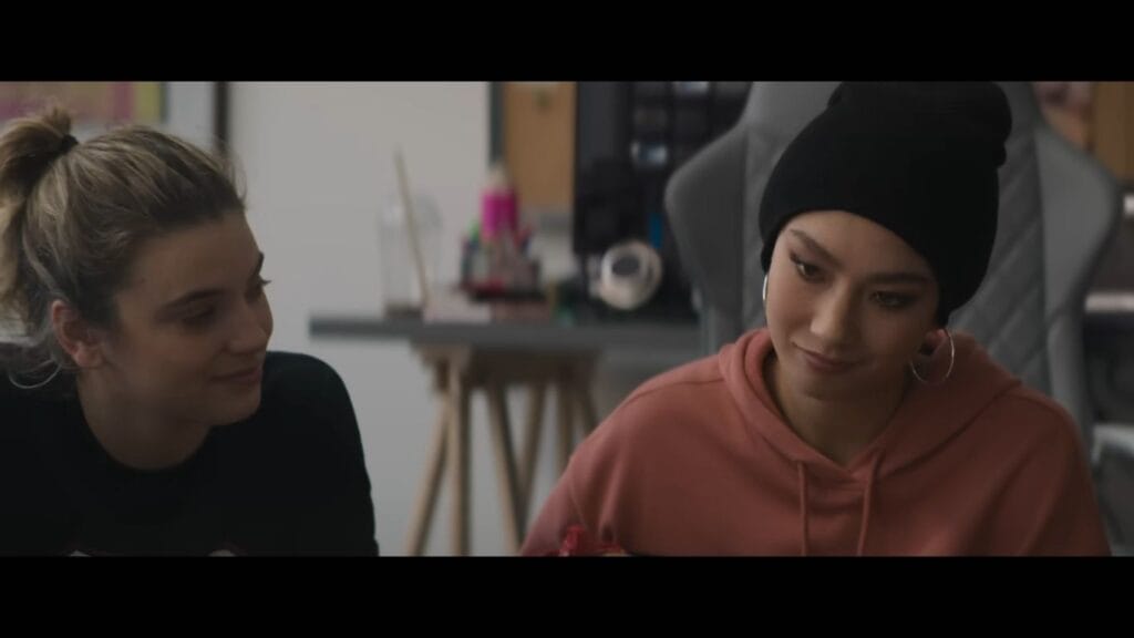 Two young women, one wearing a black beanie and peach hoodie, share a quiet, suspicious glance in a still from the supernatural thriller Do Not Enter.