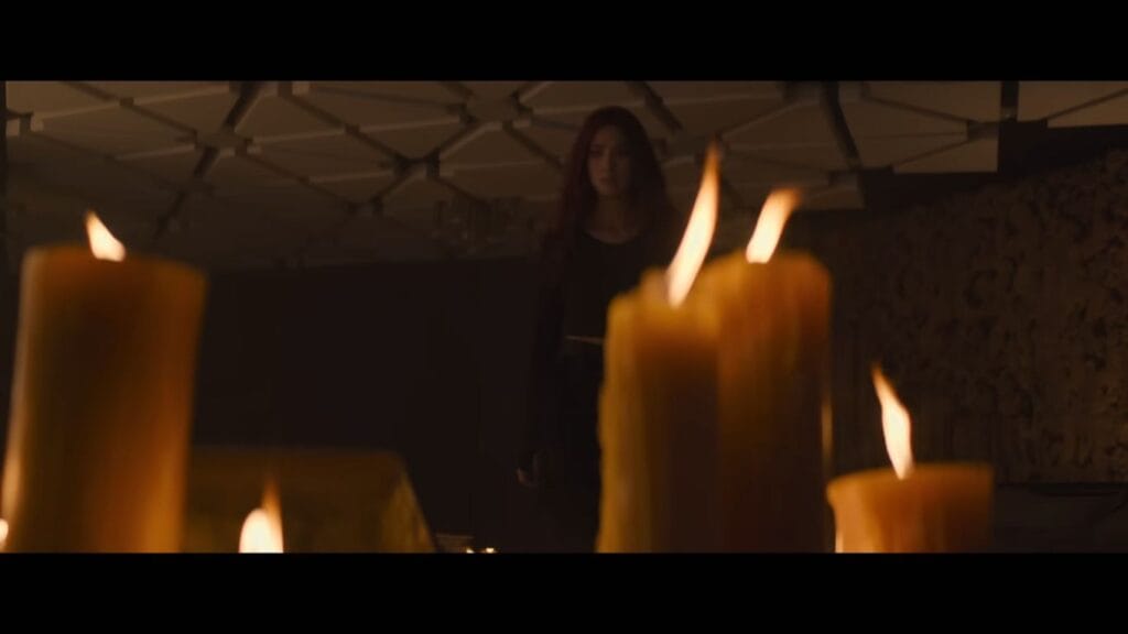 A mysterious woman stands in the background of a dark room filled with large, lit wax candles, a key atmospheric scene from Do Not Enter.