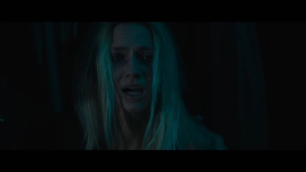A close-up of a terrified blonde woman with a tear-streaked face in a dark, blue-lit setting from the horror movie Do Not Enter (2026).