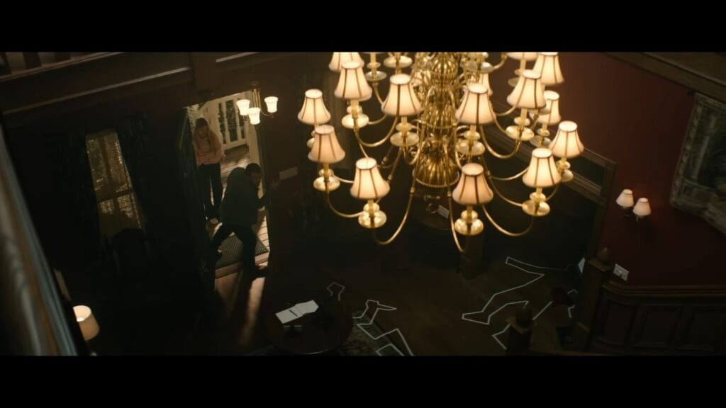 A high-angle shot of a mansion interior with a large chandelier and chalk body outlines on the floor, a pivotal scene from the Scream 7 ending.