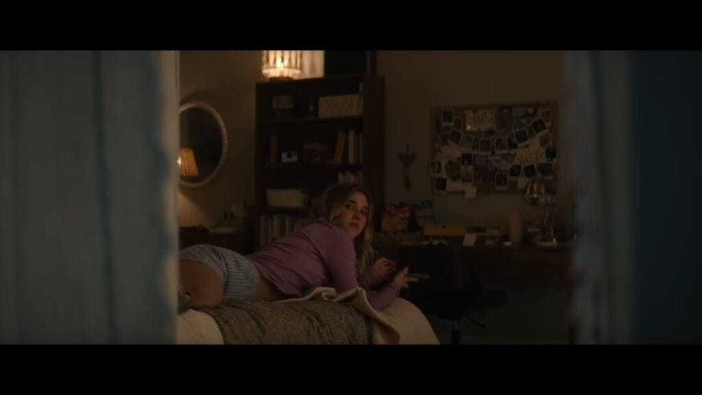 Tatum (Isabel May) lies on her bed looking back at her phone in a dark bedroom, a suspenseful moment from the horror film Scream 7.