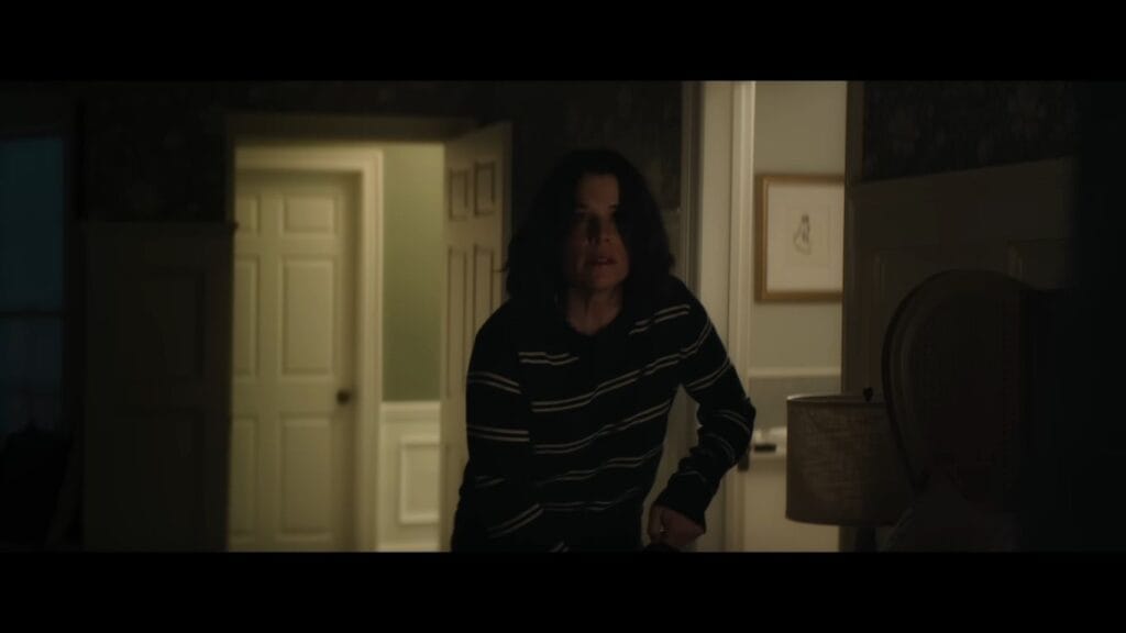 Sidney Prescott (Neve Campbell) looks alert and cautious while moving through a dark hallway in the slasher sequel Scream 7 (2026).
