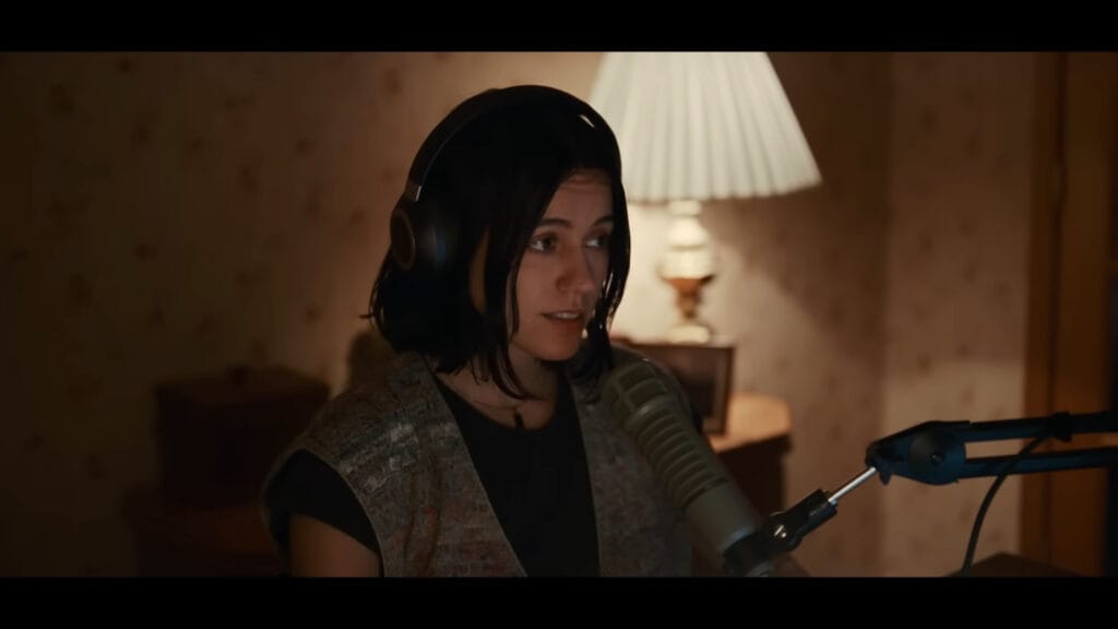 Medium shot of Evy (Nina Kiri) wearing headphones and speaking into a studio microphone.