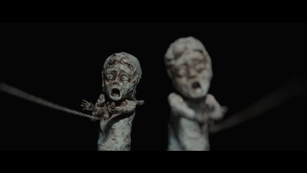 Two horrifying calcified figures bound by rusted metal chains in a dark void.