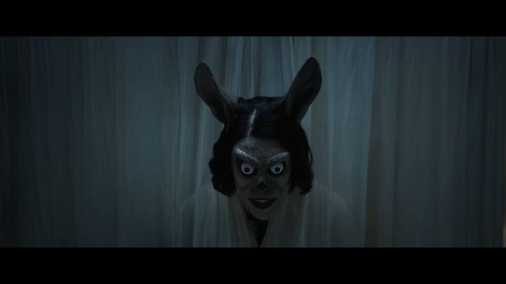 The witch with bulging eyes and animal ears peering through white curtains.