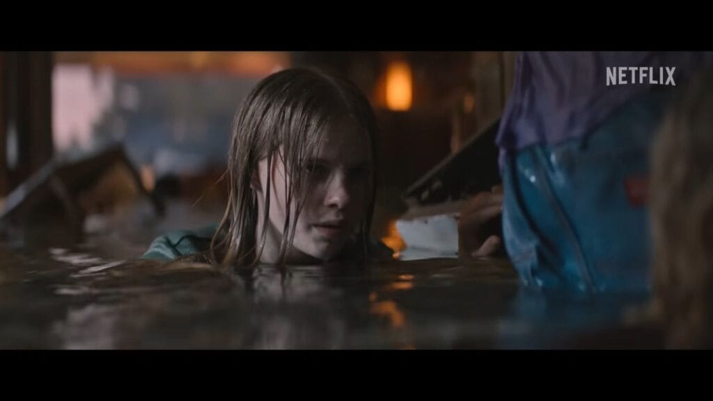 A young woman with wet hair wading through waist-deep water inside a flooded building.