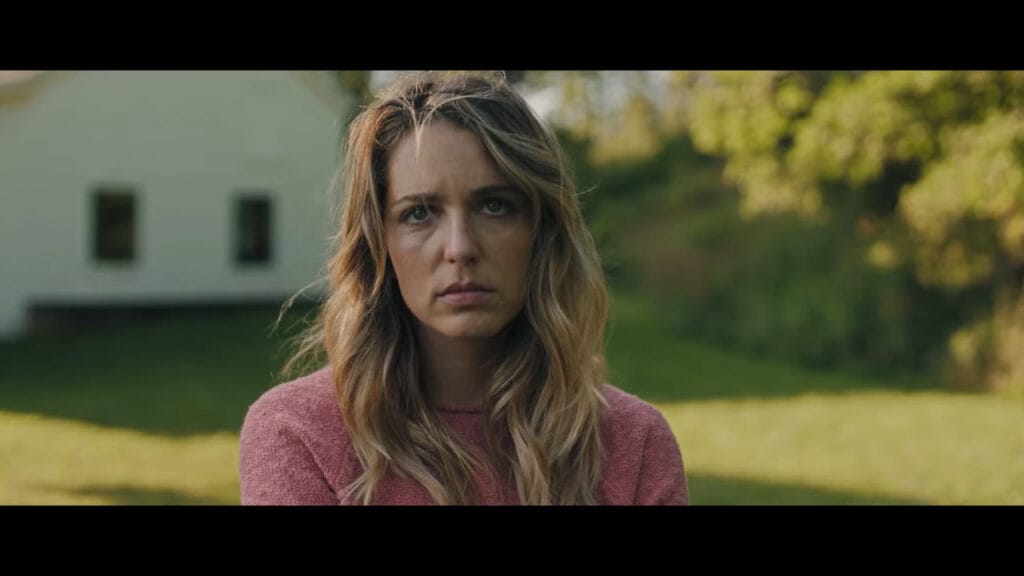 A somber close-up shot of actress Jessica Rothe looking directly forward with a serious, melancholic expression outside a house in the sci-fi horror movie Affection.