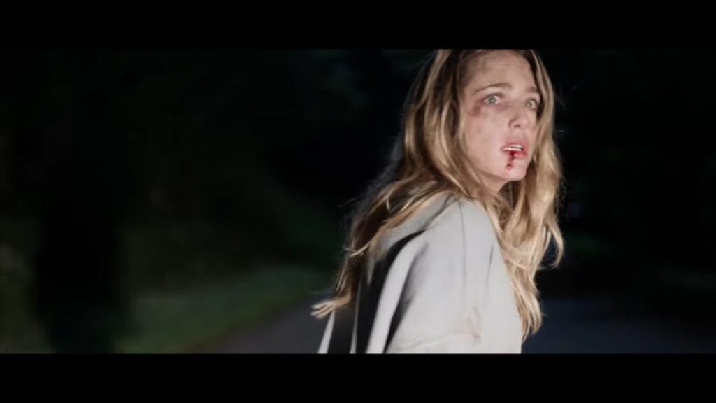 A battered and bloodied Jessica Rothe looking back in terror while fleeing down a pitch-black road at night in a scene from the horror film Affection.