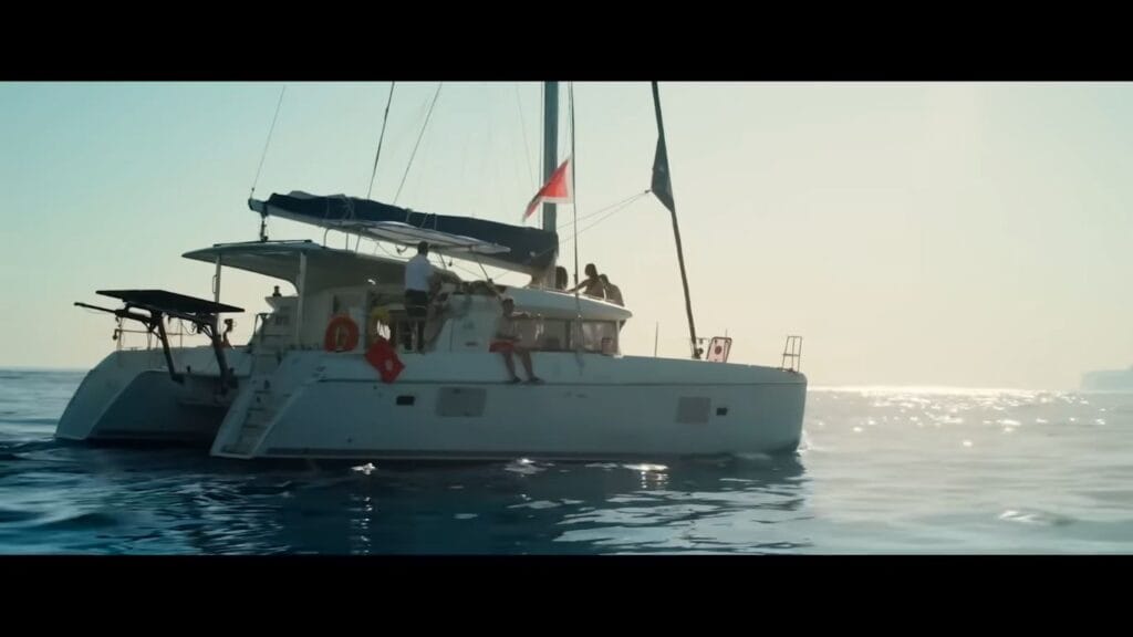 A white catamaran yacht sailing on calm blue ocean waters on a bright sunny day in a scene from the horror movie Chum.
