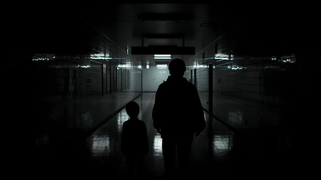 The dark silhouettes of an adult and a child standing in an eerie, pitch-black subway corridor with dim white tiles reflecting light in the J-horror movie Exit 8.