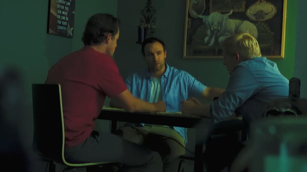 Three men sitting around a table having an intense discussion under an eerie green and blue lighting setup in a scene from the DIY horror movie Milk & Serial.