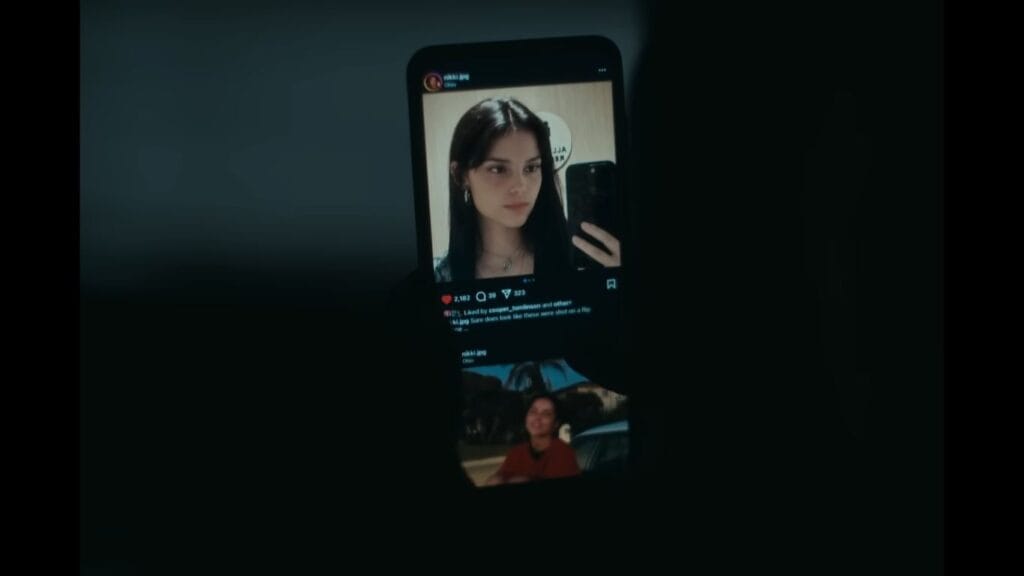 A smartphone screen in a dark room displaying a social media profile for nikki.jpg with two photos of a young woman