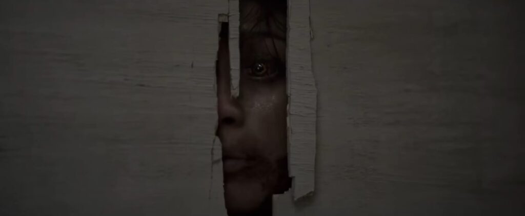 A terrifying close-up shot of a possessed Deadite with glowing eyes peering through a crack in a broken wooden door in Evil Dead Burn.
