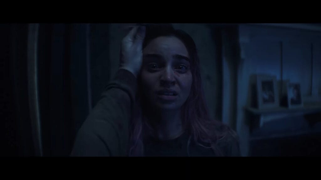 Alice holding her hand to her head with a shocked, panicked expression in a dimly lit, shadowy room in Evil Dead Burn.