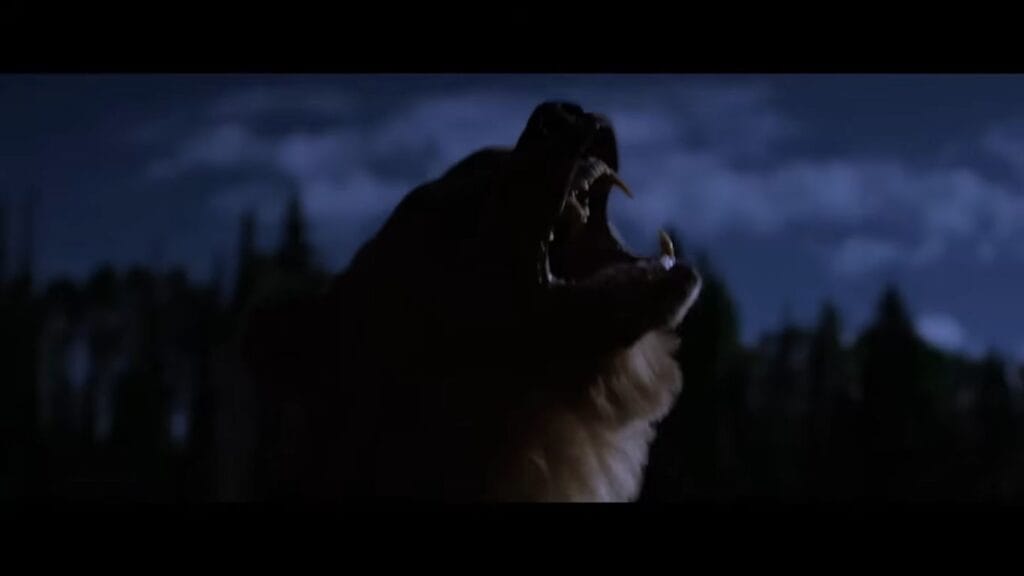 A silhouette profile shot of a large bear roaring aggressively with its mouth wide open against a dark, moody blue night sky in the survival drama Grizzly Night.
