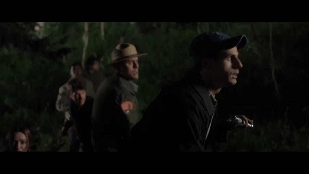 A worried night-time search party including a uniform-clad park ranger navigating through dark, dense forest brush during the film Grizzly Night.
