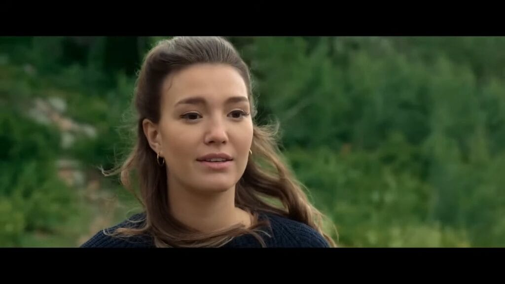 Ali Skovbye as Michelle Koons looking concerned against a blurry, lush green wilderness background in Glacier National Park from the movie Grizzly Night.