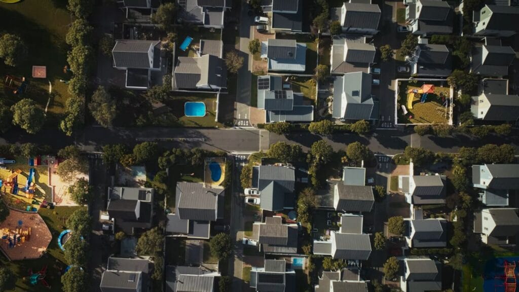 An aerial top-down drone shot of a perfectly manicured, symmetrical suburban neighborhood with houses, swimming pools, and a playground from the movie Hive.