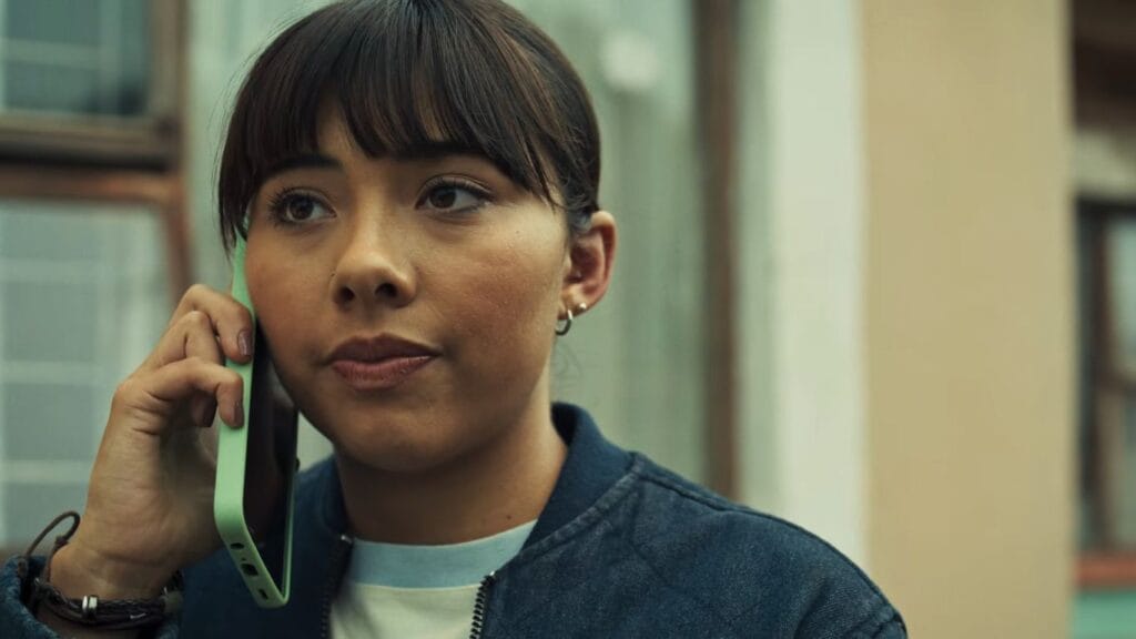 Xochitl Gomez as Sasha holding a green mobile phone to her ear with a concerned expression in a scene from the horror thriller Hive.