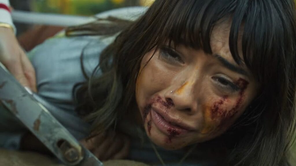 A dramatic, blood-spattered close-up of Sasha crying out in pain and terror while pinned down on the ground during a tense sequence from Hive.