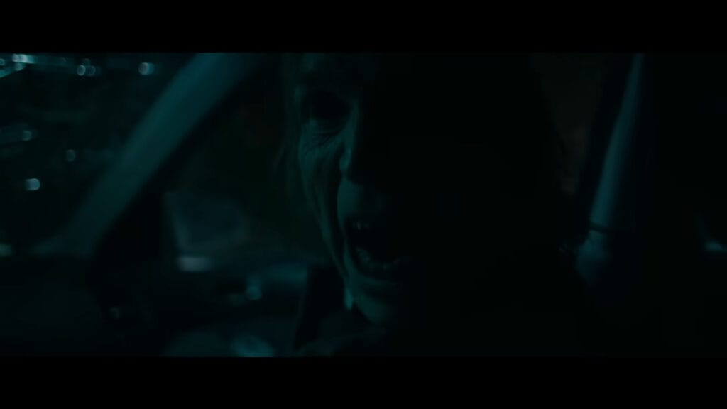 A dark, unsettling close-up shot of a demonic figure aggressively shouting inside a vehicle during André Øvredal's Passenger.