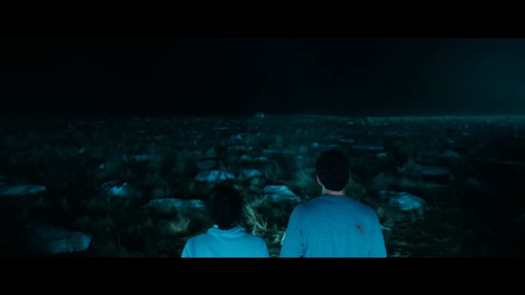 A wide, dark cinematic shot showing Tyler and Maddie from behind as they look out over a vast field filled with debris during the climax of Passenger.