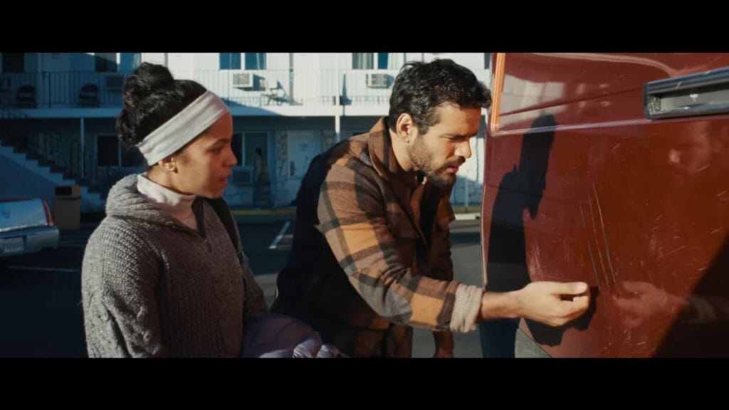Tyler and Maddie looking concerned while inspecting long, deep scratch marks on the side of their red home van in a scene from the horror movie Passenger.