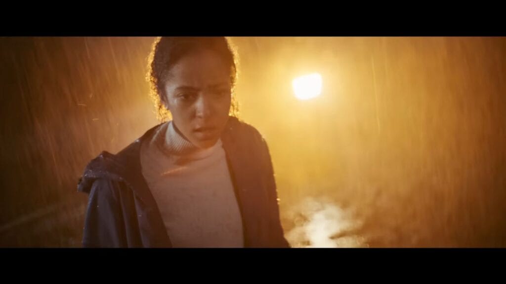 Actress Lou Llobell as Maddie looking terrified and soaked under a heavy, backlit downpour of rain at night in André Øvredal's Passenger.