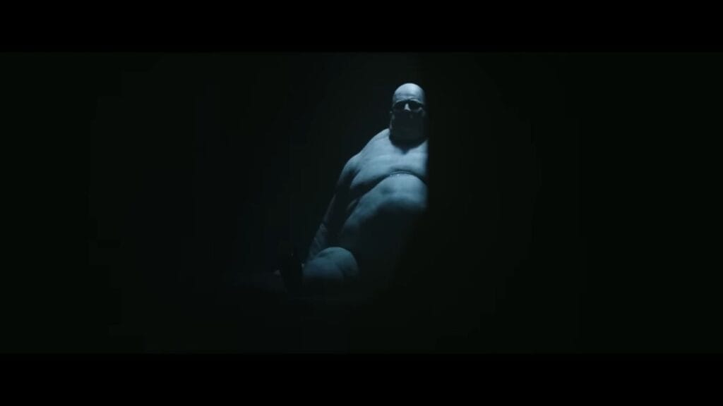 A pale, muscular, bald creature crouching in the dark shadows in Resident Evil