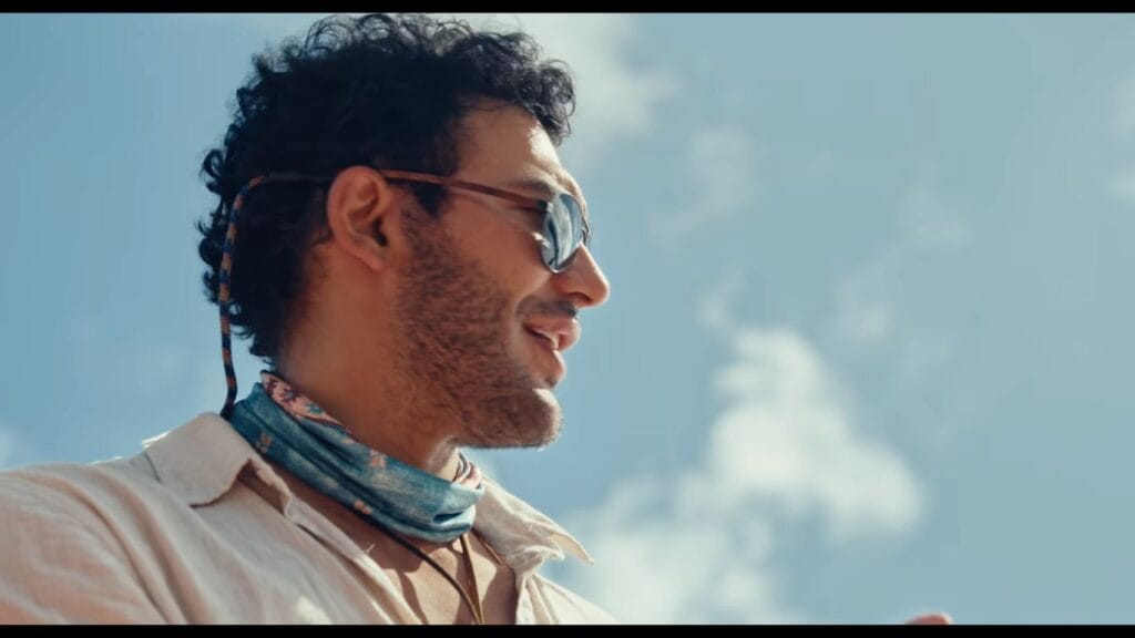 Alexander Wraith as Mandal wearing sunglasses and a neck gaiter smiling against a clear blue sky in Phil Volken's aquatic thriller The Bay.