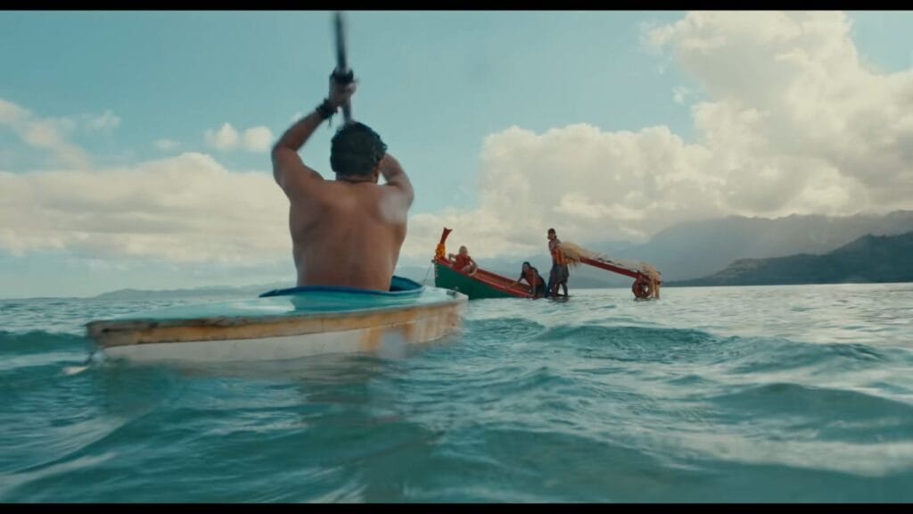 A man paddling a small kayak toward a sinking wooden boat anchored in open water under a bright sunny sky in a scene from The Bay.