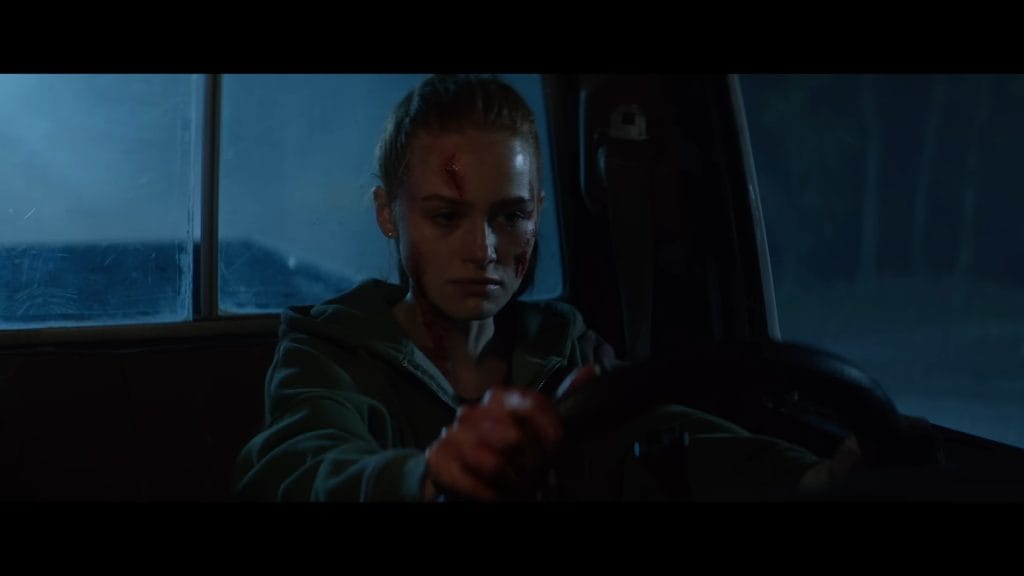 Madelaine Petsch as a bloodied, bruised Maya gripping the steering wheel of a vehicle at night in a high-tension scene from The Strangers: Chapter 3.